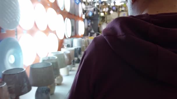 En man väljer en elektrisk lampa för att lysa upp ett rum. Shopping på en järnaffär, sälja varor, bakgrund — Stockvideo