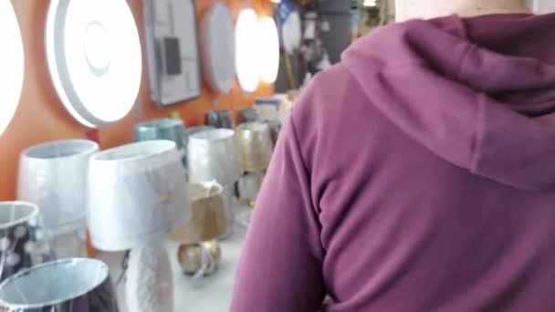 Een man kiest een elektrische lamp om een kamer te verlichten. Winkelen in een ijzerwinkel, verkopen van goederen, achtergrond — Stockvideo
