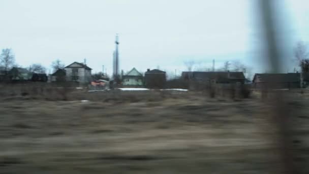 Вид из окна поезда во время езды по сельской местности и деревне. Весеннее время, оттаявшие участки со снегом, фон. Пейзаж — стоковое видео