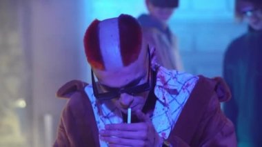 Siberpunk gelecek konsepti. Punk tarzı saç kesimi olan tuhaf bir tip. Gece şehirde ışıklı sigara içiyor. Suçlu haydut. Bilim kurgu sahnesi, fantezi. Yarının Dünyası