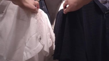 Bir erkek dükkanda kıyafet seçer, alışveriş yapar. Mağazada tişört ve ceket seçimi, arka plan, yakın plan