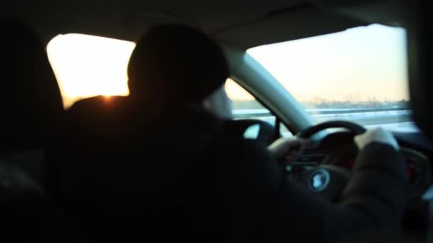 Conducente di sesso maschile alla guida di una macchina moderna la sera in inverno sullo sfondo di un tramonto soleggiato. Concetto di viaggio e avventura in auto, autostrada — Video Stock