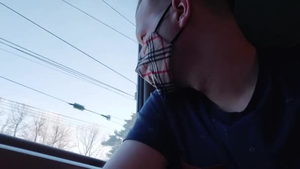 Een jonge man met een beschermend medisch masker rijdt in een trein en kijkt uit het raam. Concept van bescherming en reizen tijdens de COVID-19 pandemie, passagier — Stockvideo