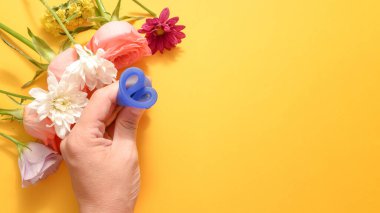 Kadın elinde katlanmış bir adet kupası tutuyor sarı bir arka planda çiçekli.