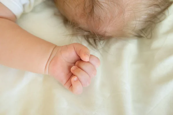 Närbild baby knytnäve och krona med blont hår på den vita filten — Stockfoto