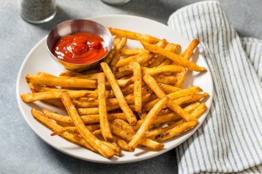 Ev yapımı baharatlı patates kızartması ve ketçaplı tabak.