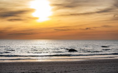 Kumsalda ve denizde bulutlu gün batımı