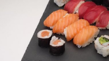 Suşi tipik Japon Asya yemekleri. Nigiri somonu, ton balığı, hosomaki, uramaki beyaz arka planda bir tabakta dönüyor..
