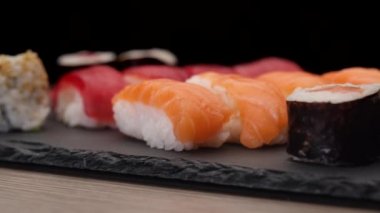 Suşi çeşitleri siyah arka planda bir tabakta dönüyor. Nigiri somonu, ton balığı, hosomaki, uramaki. Tipik Asya Japon yemekleri..