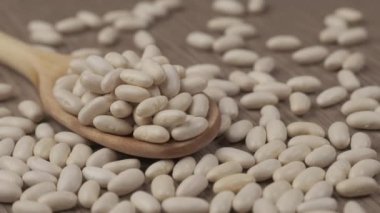 White dry beans rotating on wooden spoon. Healthy nutrition Mediterranean diet, vegan vegetarian ingredient