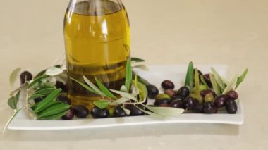 Extra virgin oil in a bottle, red and black olives in the background. Typical Mediterranean Italian food. Healthy ingredient display. Tilting shot.