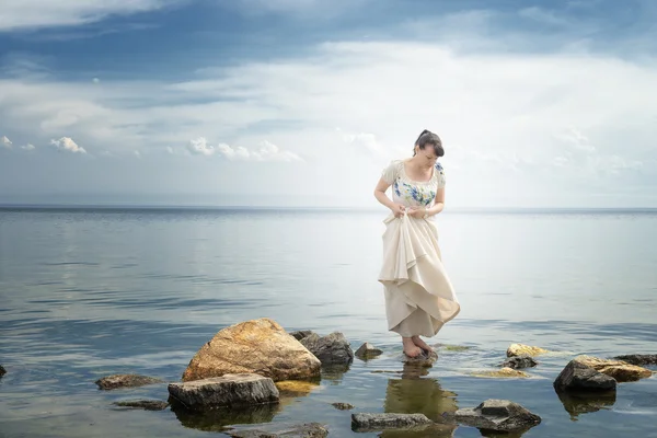 Flicka stöder en klänning på stenar. Bajkalsjön Royaltyfria Stockfoton