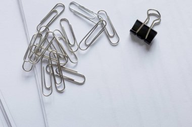 Beyaz kağıt üzerine ataç, ataç düzenleme, metal ataçlar ve beyaz kağıda yerleştirilmiş siyah bir ataç, kırtasiye, ofis organizasyonu ve temiz çalışma alanı gereksinimleri, Top view