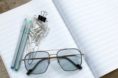 Çizgili bir defterde gözlüklü kırtasiye malzemeleri, çalışmayı, ofis işini ve basit bir çalışma alanını temsil ediyor.