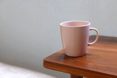 Ahşap bir masada doğal ışıkta pembe seramik bardak kahve, çay fincanı ve içecek için boş pembe bardak sıcak ve sade bir minimalist ev atmosferi yaratıyor.