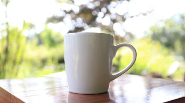 Açık havada, beyaz kahve fincanı ve doğal bokeh arka planı. Rahatlatıcı sabah kahve konsepti, minimum yaşam tarzı, sakin atmosfer ve doğa ışığı