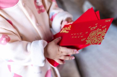 Sevimli bir bebek kırmızı bir ang pao zarfı tutuyor. İçinde altın detaylar var. Ay Yeni Yılı 'nda veya Çin Yeni Yılı' nda şans, bereket ve refahı simgeliyor.