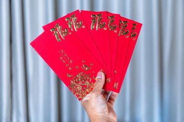 Yeni Yıl Kutlaması için Altın Çin Sembolleri içeren kırmızı zarf, kırmızı bir zarf tutan el. Geleneksel Ay Yeni Yılı selamlaması, Şansın, refahın ve şenlikli kutlamaların sembolü