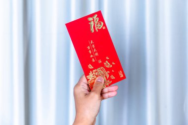 Yeni Yıl Kutlaması için Altın Çin Sembolleri içeren kırmızı zarf, kırmızı bir zarf tutan el. Geleneksel Ay Yeni Yılı selamlaması, Şansın, refahın ve şenlikli kutlamaların sembolü