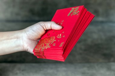 Elinde altın (Fu) sembollü kırmızı zarflar, şans, refah ve Çin Yeni Yılı kutlamalarını temsil ediyor.
