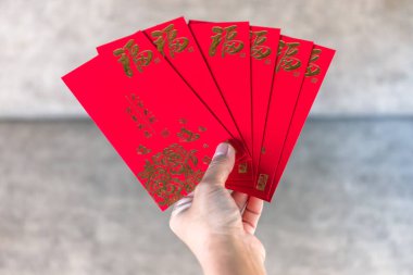 Yeni Yıl Kutlaması için Altın Çin Sembolleri içeren kırmızı zarf, kırmızı bir zarf tutan el. Geleneksel Ay Yeni Yılı selamlaması, Şansın, refahın ve şenlikli kutlamaların sembolü