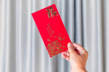 Yeni Yıl Kutlaması için Altın Çin Sembolleri içeren kırmızı zarf, kırmızı bir zarf tutan el. Geleneksel Ay Yeni Yılı selamlaması, Şansın, refahın ve şenlikli kutlamaların sembolü
