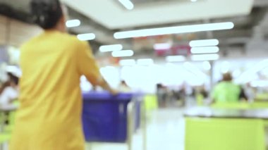 İnsanlar ve parlak yeşil sandalyelerle dolu bir alışveriş merkezinin bulanık görüntüsü, canlı, modern bir kapalı alan atmosferi yaratıyor.