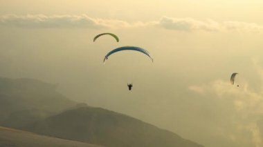 Bulutlu gökyüzünde paraşütçülerin silueti yükseliyor.