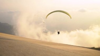 Paraglider gün batımında dağda yamaç paraşütü sporu yapıyor.