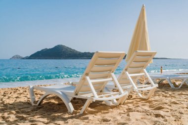 İki plaj sandalyesi ve şemsiye güzel kumsalda birinin gelip dinlenmesini bekliyor. Seyahat, tatil ve tatil konsepti.