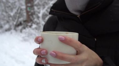 Kadın kupayı elinde buharda pişmiş çayla kış ormanında karın içinde tutuyor.