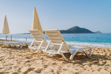 Boş plaj sandalyeleri ve sarı güneş şemsiyesi mavi denizin arka planında turistleri bekliyor. Güzel sahil tatil köyü..