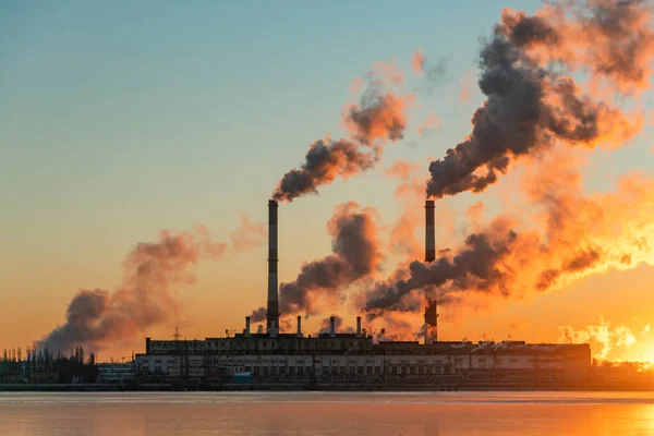 Smoke from chimney factory at sunrise. Pollution by industry smokestack against a red sunrise