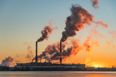 Endüstriyel bir şirketin boruları. Atmosfere ve kirliliğe duman salınımı. Kızıl gökyüzü gün doğumunda