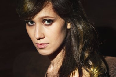 Koyu arkaplanda uzun kıvırcık saçlı güzel bir kadının yüzü. Dalgalı saç stili olan manken. Makyajlı kadın yüzü.