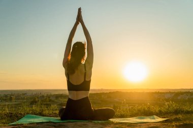 Doğada gün batımıyla yoga yapan genç bir kadın. Sağlıklı ve Yoga Konsepti