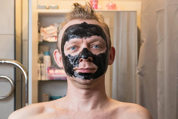 Men receiving facial black mask in the bathroom, skin problems, care man in home concept