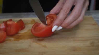 Kadın olgun bir domatesi tahta bir kesme tahtasıyla kesiyor. Kadın eli ev mutfağında sağlıklı sebze salatası hazırlıyor.