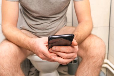 Evdeki klozette ishal olan bir adam akıllı telefon kullanıyor.