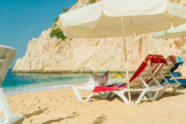 Yaz günü Kaputas Sahili 'nde plaj havluları, çantaları ve şemsiyeleri olan şezlonglar, Türkiye tatili