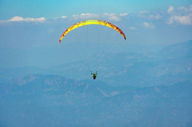Paraglider dağda gökyüzünde yamaç paraşütü yaparak yükseliyor. Dağlarda ekstrem spor