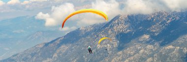 Paraglider dağda gökyüzünde yamaç paraşütü yaparak yükseliyor. Dağlarda inanılmaz bir spor. Geniş pankart