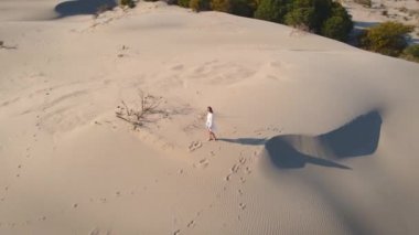 Çölde dalgalı kum tepelerinde yürüyen bir kadın.
