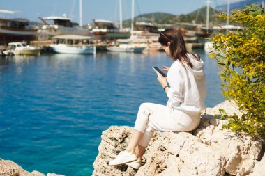 Kadınlar deniz kıyısında otururken akıllı telefon kullanırlar. Sosyal ağda tatilde olan bağlantı arkadaşı