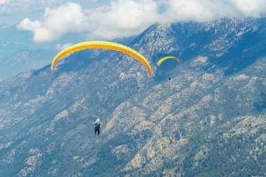 Paragliderler dağda gökyüzünde yamaç paraşütü yaparak süzülüyorlar. Dağlarda ekstrem spor