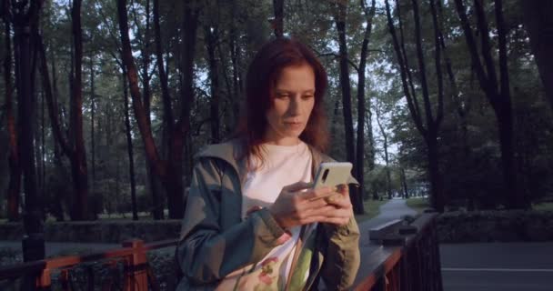 Тысячелетняя Женщина Прогулке Парке Используя Свой Смартфон Доступа Социальным Сетям — стоковое видео