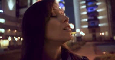 Milenyum kadını gece şehir binasına bakıp esnemekten yoruldu. Büyük şehirde yorgun gece yürüyüşü.