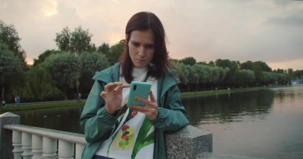 Millennial Woman bei einem Spaziergang im Park mit ihrem Smartphone — Stockvideo