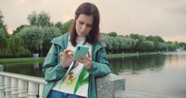 Millennial Woman sosyal ağlara erişmek için parkta akıllı telefonunu kullanıyor. Her yerde bağlı kalmak