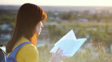 Kitabı olan genç bayan doğada dinleniyor ve gün batımında kitap okuyor, dinleniyor ve tatilin tadını çıkarıyor.